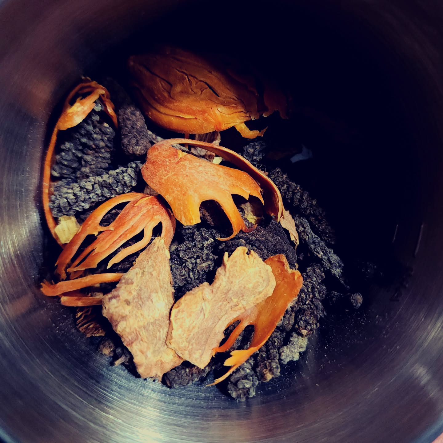 A grinder cup containing whole spices including mace and long pepper