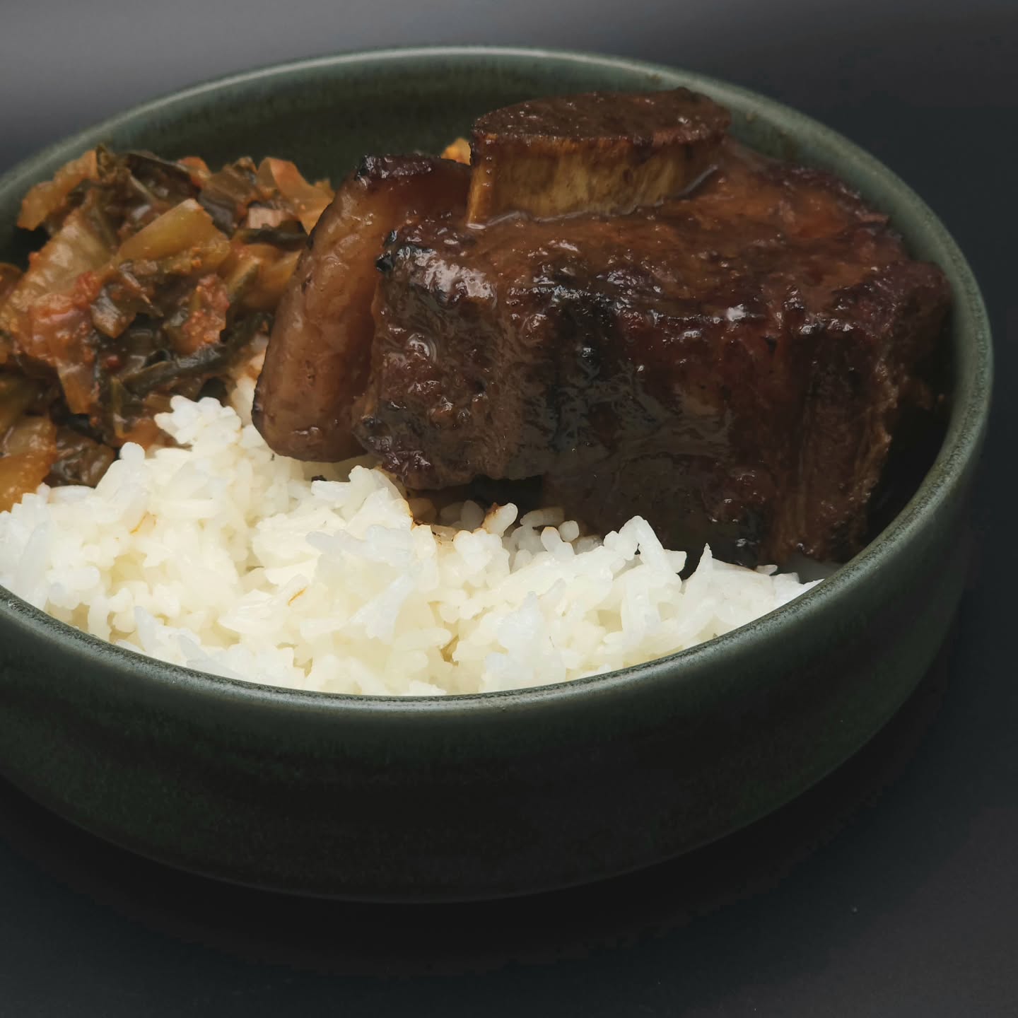 Green porcelain bowl containing rice, meat, and vegetables.