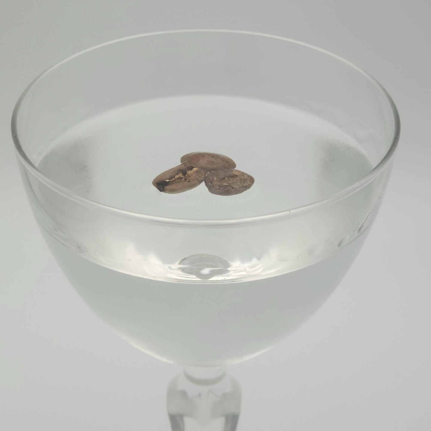 Crystal-clear drink in a Nick and Nora with three coffee beans floating on top.