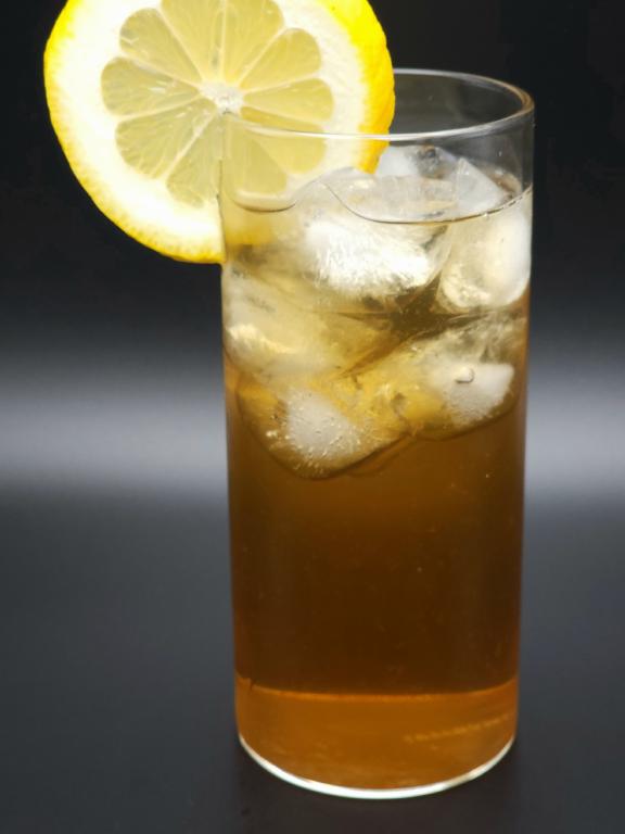 gin fizz glass filled with ice and amber liquid, garnished with a lemon wheel