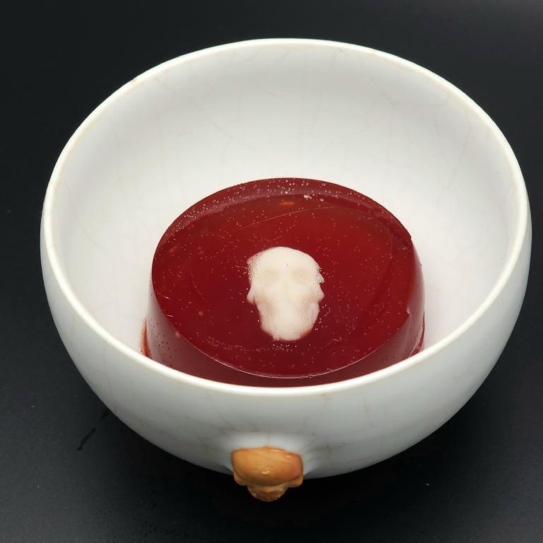white teacup with a molded jelly placed in the bottom. The jelly appears red but has a white skull clearly visible within it.